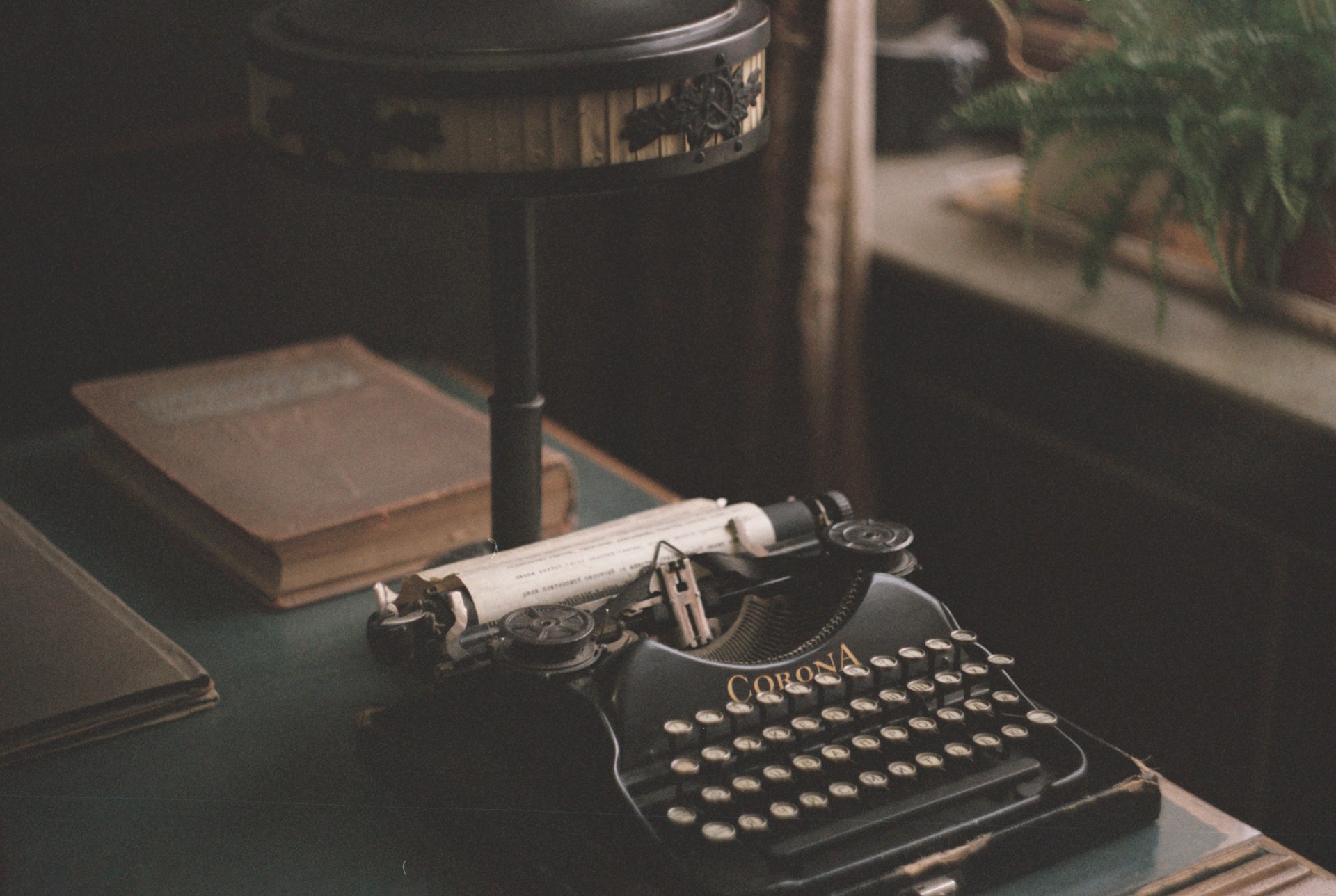 A typewriter on an old desk next to a dusty book.